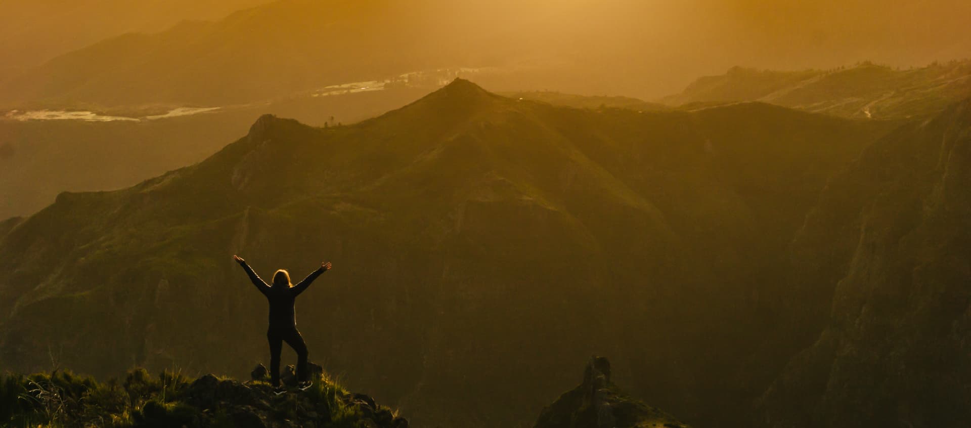Osoba stojąca na górskim szlaku o zachodzie słońca